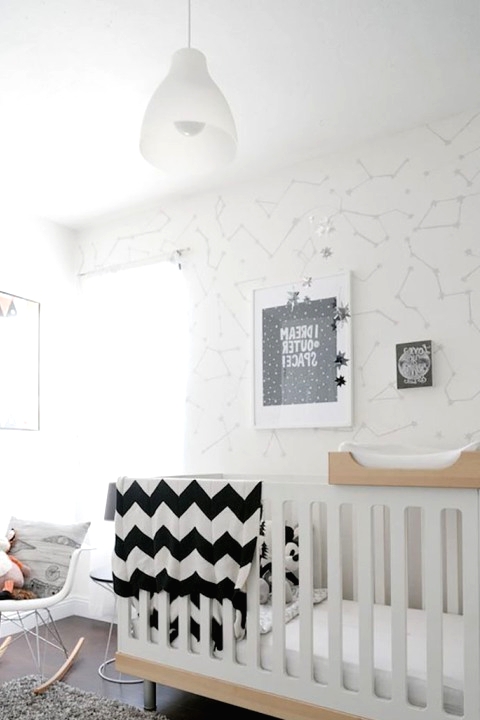 an inviting Scandi nursery with wallpaper walls, a white and stained crib, a rocker, a grey rug and some monochromatic bedding