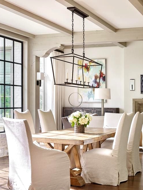 a beautiful vintage farmhouse dining room with neutral walls and greige wooden beams, a wooden dining table, upholstered chairs and a chandelier