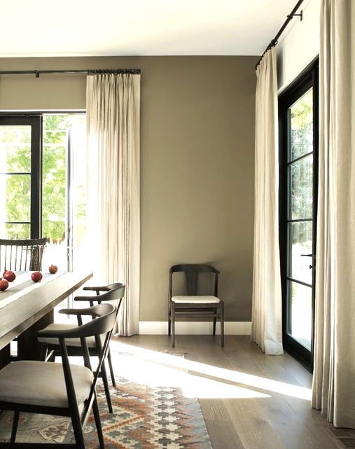 a greige dining room with a black long dining table, neutral and black chairs, neutral curtains, a bold printed rug is a lovely space to have a meal