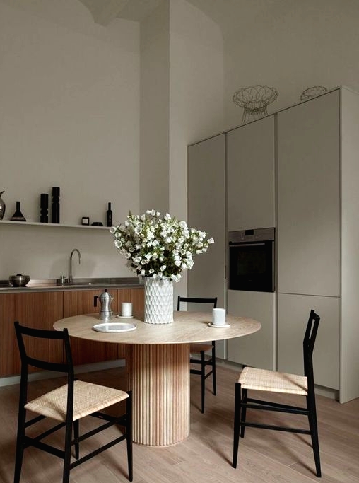 a greige kitchen combined with a kitchen, light-stained furniture, a round table and woven chairs, a grey storage unit, a long shelf and some blooms