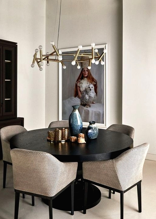 a pretty greige dining room with a dark stained storage unit, a black round table, greige chairs, a gilded chandelier and a large and bold artwork