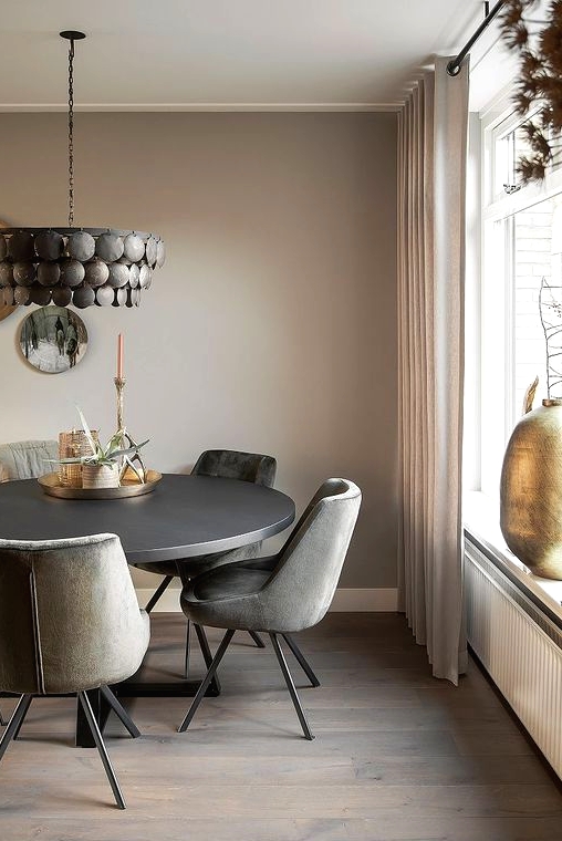 an elegant and refined greige dining room with a black round table, grey chairs, a black metal chandelier, decorative plates and a candle