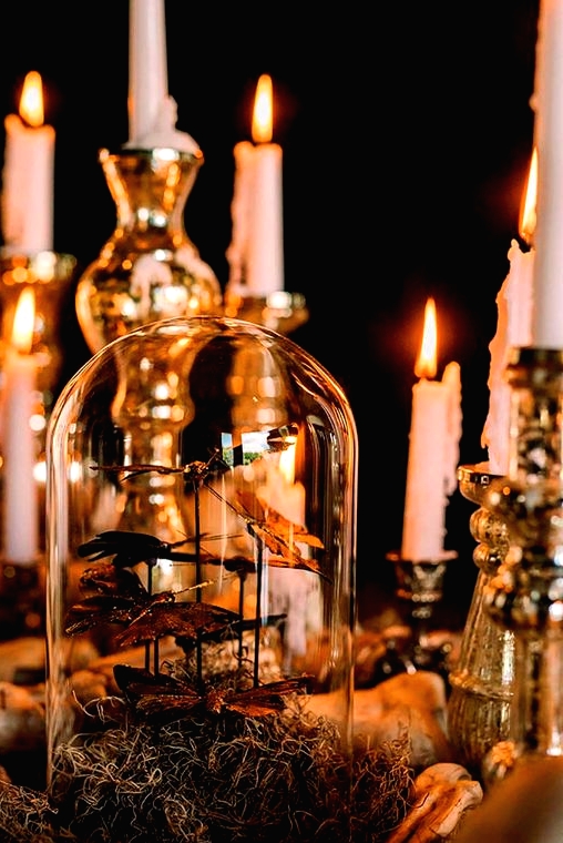 a vintage Halloween decoration of a cloche with faux butterflies, candles in gilded candlesticks, hay is chic