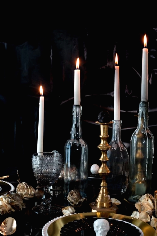 an elegant vintage Halloween tablescape with black and gold plates, tall candles in bottles, chic glasses and dried blooms on the table