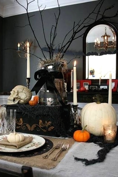 a lovely vintage Halloween tablescape with neutral linens, a black table runner, a black chest with a branch arrangement on top, skulls, pumpkins and tall candles