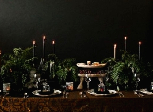 a Halloween tablescape with a rust printed tablecloth, black and white candles, lots of greenery and refined plates and glasses