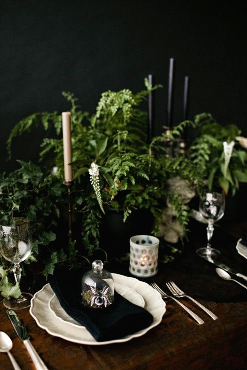 a fresh vintage Halloween tablescape with lots of greenery, black and white candles, white candleholders, porcelain and metallic cutlery is cool