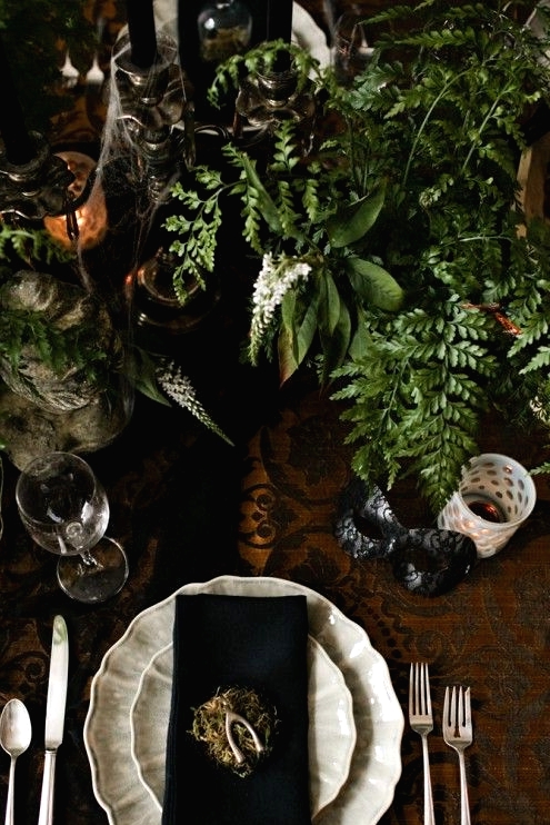 a vintage Halloween table setting with black and white touches, greenery, black candles in vintage candleholders, spiderwebs and hay is a creative idea