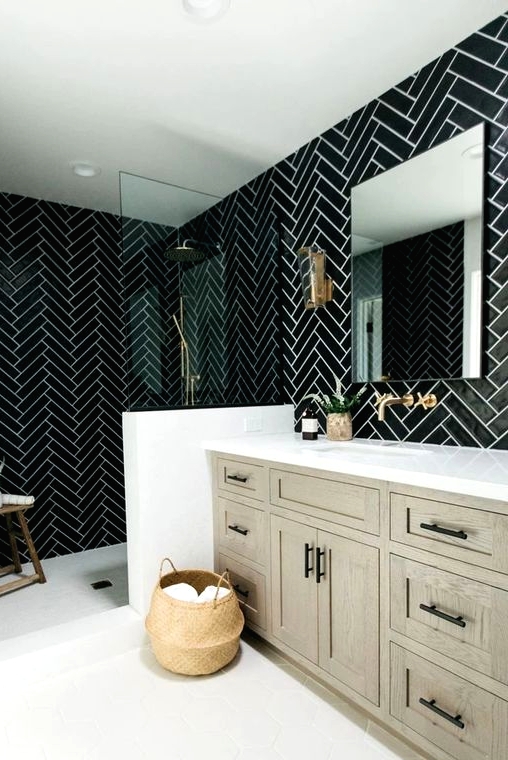 a chic black and white bathroom with chevron tiles, a greige wooden vanity, black fixtures and a wooden stool plus a basket for storage is cool