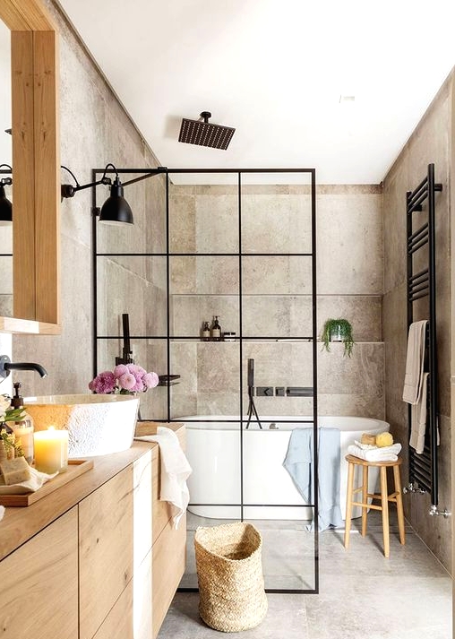 a greige bathroom clad with concrete, with a light-stained vanity and a large mirror, a shower space with a black space divider and black fixtures