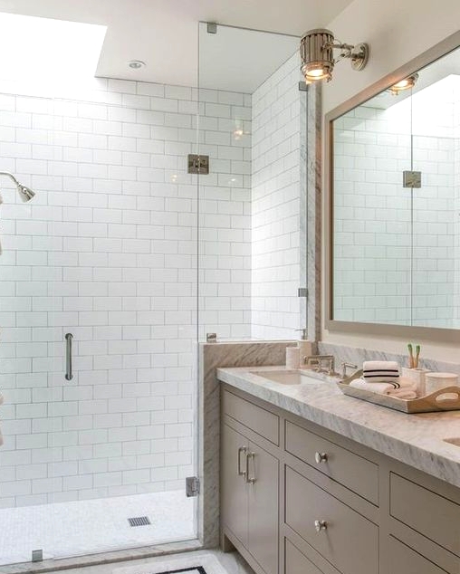 a pretty neutral bathroom clad with subway tiles, with a greige vanity with a white stone countertop and a skylight over the shower