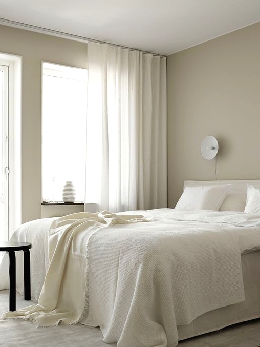 a serene bedroom with greige walls, creamy and black furniture, creamy bedding and curtains plus lots of natural light incoming