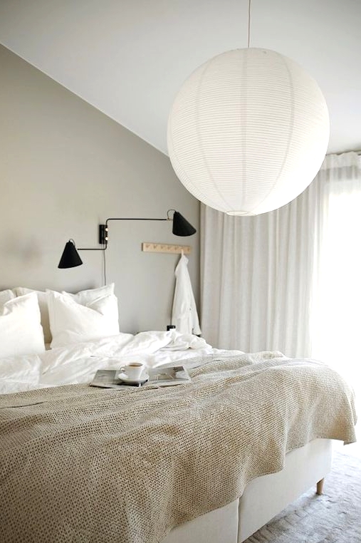 an ethereal greige bedroom with a creamy bed, a black sconce, a pendant lamp and neutral textiles is welcoming