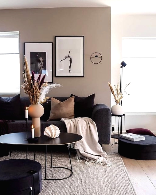 a greige living room with black seating furniture, a black coffee table, a mini gallery wall, black and tan pillows, a terracotta vase and some grasses