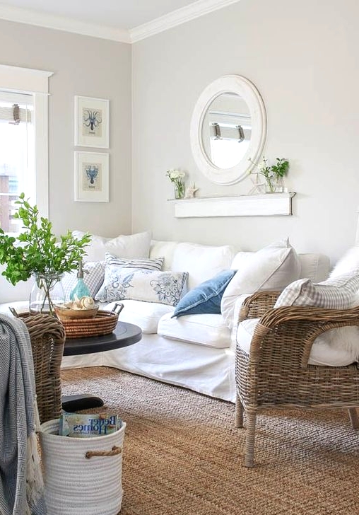 a lovely greige farmhouse living room with a white sectional, woven chairs, a mini gallery wall, a round mirror and printed pillows