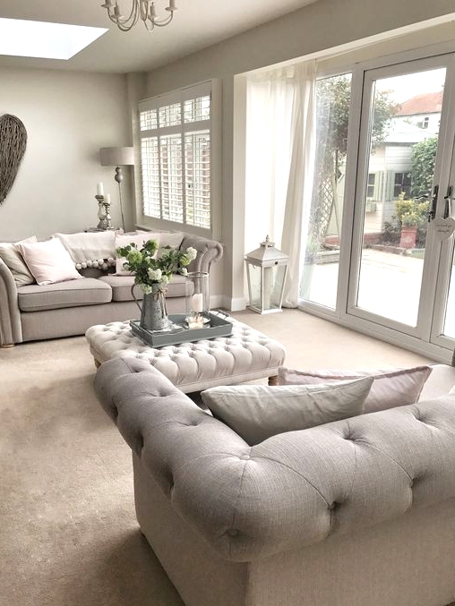a pretty greige living room with matching tufted sofas, a tufted ottoman, a chandelier, a driftwood heart and some elegant floor and table lamps