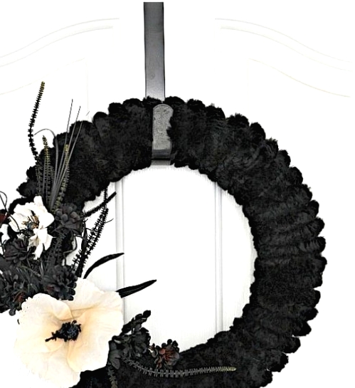 a refined black faux fur Halloween wreath with black faux blooms, grasses and leaves plus a single white flower is a very elegant idea