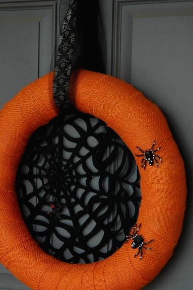 a bright Halloween wreath of an orange form, with a black spider net inside and some faux spiders on the wreath is Halloween classics