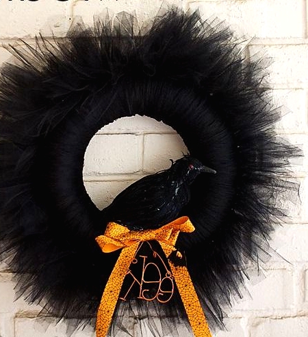 a black Halloween wreath with much black tulel around, with a faux blackbird and an orange bow plus some letters is a stylish decoration for Halloween