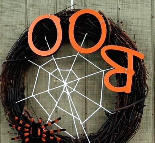 a stylish Halloween wreath of vine,w ith orange letters, a spider net and a large and bold spider is a geat idea for Halloween