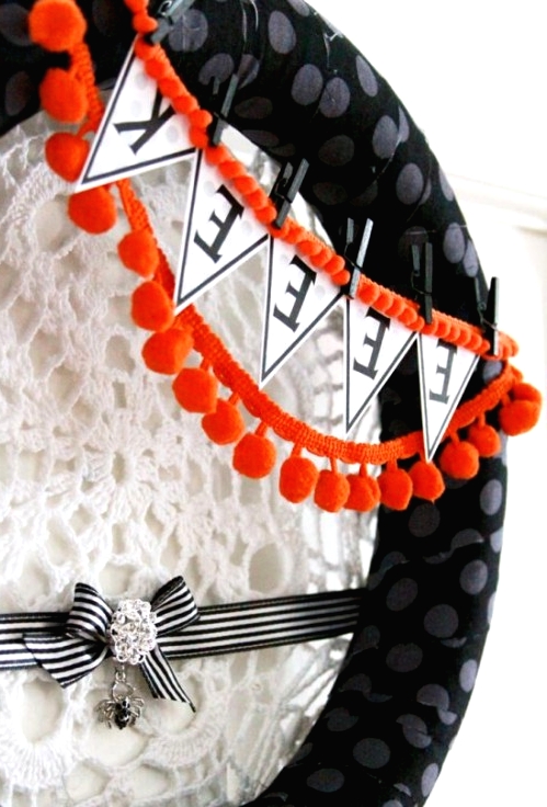 a black polka dot Halloween wreath with a bunting and orange pompoms, a doily spider net and a stripe ribbon with a bow and a spider pendant is a lovely idea to rock