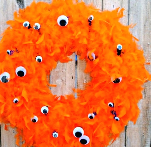 a bold orange feather wreath with googly eyes all over is a lovely and bright idea for Halloween decor