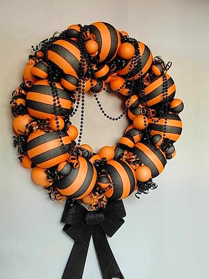 a colorful black and orange Halloween wreath of plastic balls, ornaments, black beds, swirls and a black glitter bow