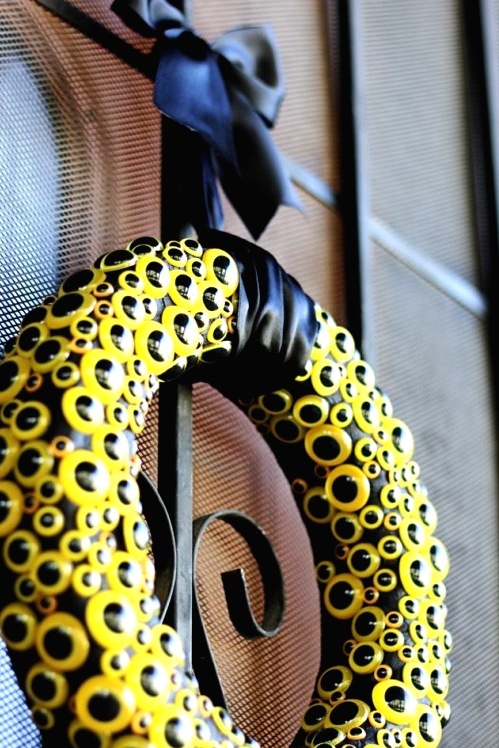 a black Halloween wreath covered with yellow googly eyes and with a black bow is a very bold and fresh modern decor idea