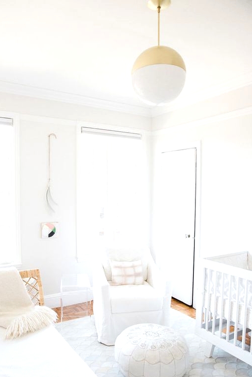 a clean white contemporary nursery with cool furniture, a Moroccan ottoman, a gold and white pendant lamp and neutral textiles