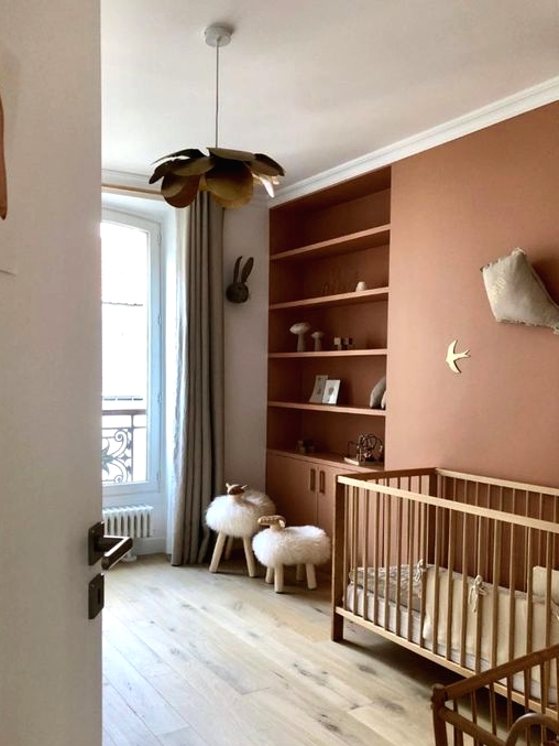 a lovely contemporary nursery in muted color, with a rust accent wall and built-in shelves, stained cribs, faux fur stools and grey curtains