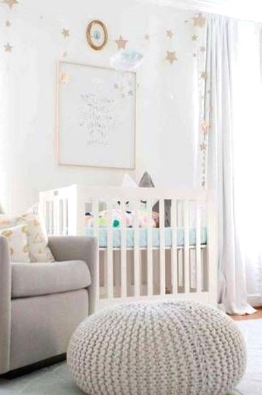 a neutral nursery with a star accent wall, a white crib with star pillows, a grey chair and a chunky knit pouf and star buntings is cool