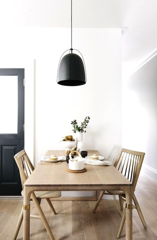a laconic Nordic dining room with a sleek stained table and chairs, a black pendant lamp and greenery is super cool