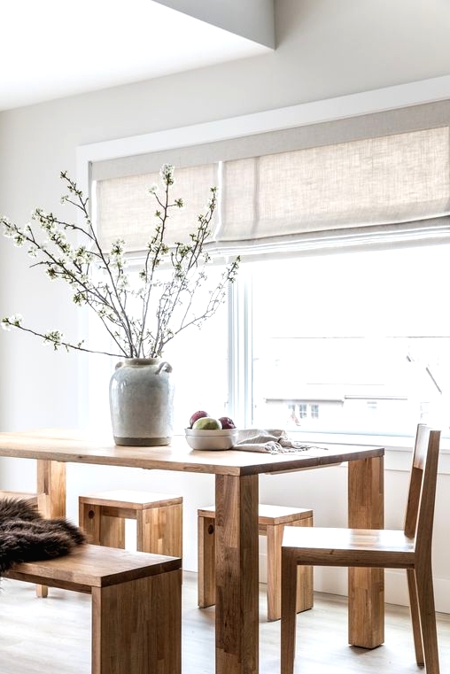 a Nordic dining room with a wooden dining table, chairs, benches, neutral shades and a grey vase with blooming branches