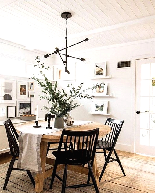 a pretty modern Nordic dining room with a round stained table, black chairs, a chandelier, a gallery wall and ledges with art