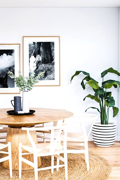 a pretty Nordic dining space with a round stained table, woven chairs, a jute rug, a mini gallery wall and a potted plant
