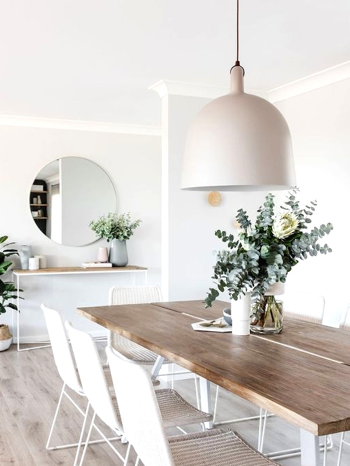 a refined Scandinavian dining room with a sleek table, white woven chairs, a tan pendant lamp and potted plants