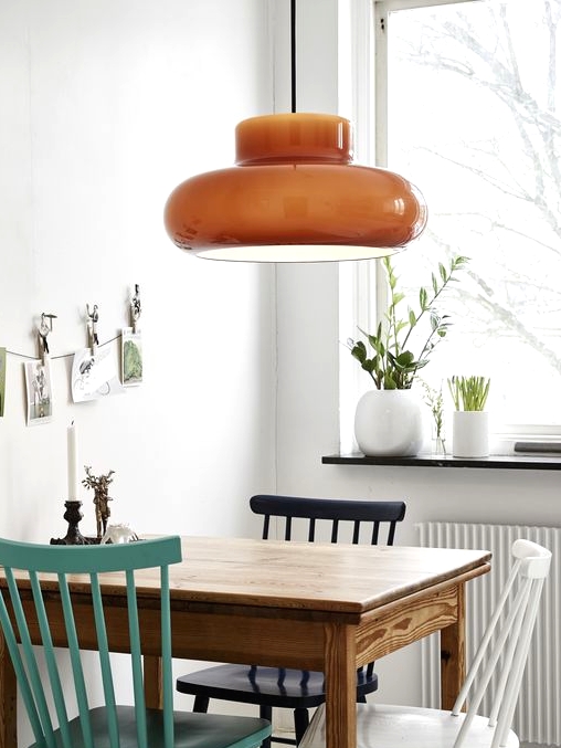 a small and cool Nordic dining space with a stained table, a white, turquoise and black chair, an orange pendant lamp