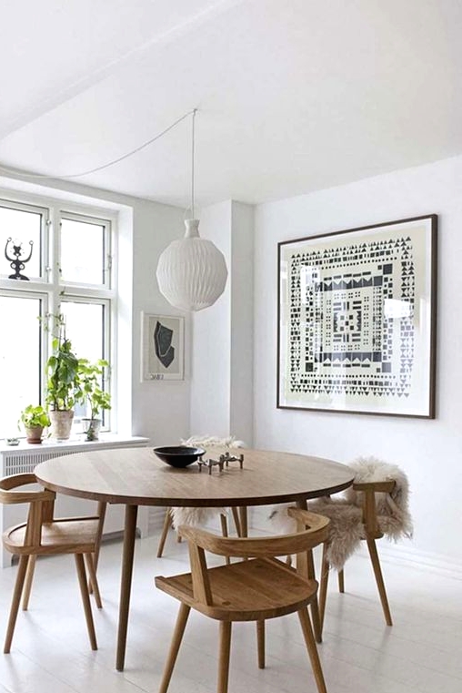 an airy Scandinavian dining nook with a round table and matching wooden chairs, a statement artwork and a pendant lamp