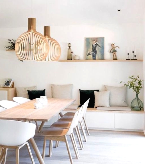 an airy Scandinavian dining space with a sleek storage bench, a light-stained table, matching white chairs, plywood pendant lamps