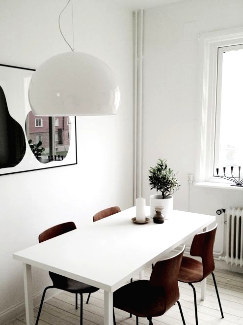 a small modern Scandi dining nook with a statement artwork, a white table, plwywood chairs and a white pendant lamp