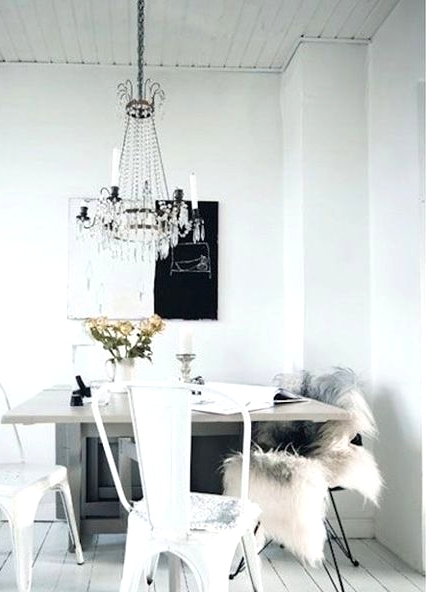 a pretty Scandinavian dining room with a table with a stone tabletop, mismatching black and white chairs, a statement artwork and a crystal chandelier