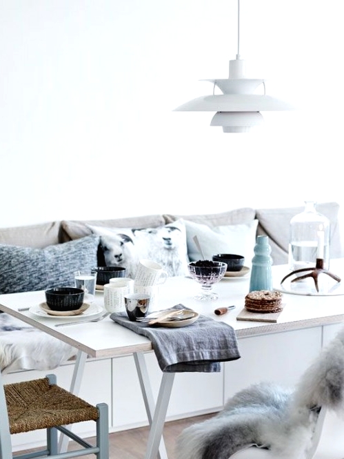 a serene and fresh Scandinavian dining space with a sleek storage bench, mismatching chairs, a simple IKEA table and lots of soft pillows and cushions