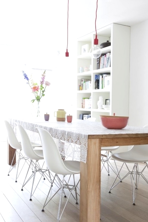 a Nordic dining room with a white bookcase, a light-stained wooden dining table, white chairs and pendant bulbs over the space