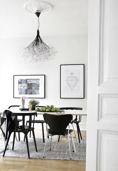 a stylish Scandinavian dining room with a white table, black chairs and a green one for an accent, a small gallery wall and a bubble chandelier