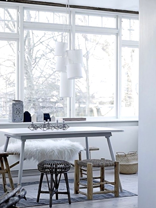 an ethereal Scandinavian dining room with a white dining table, mismatching wooden stools and a bench, a cluster of pendant lamps and some baskets for storage