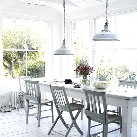 a whitewashed Scandinavian dining room with a long white table, mismatching whitewashed wooden chairs, white pendant lamps and views of the garden