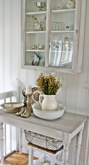 a whitewashed storage cabinet with a glass door and matching furniture items for a small and cozy shabby chic nook