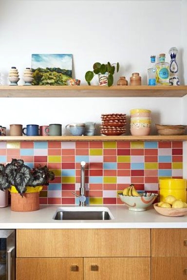 a light-stained modern kitchen with white stone countertops and a colorful tile backsplash in pink, red, blue and yellow that creates a mood in the space