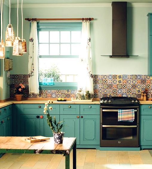 a teal kitchen with vintage cabinets, butcherblock countertops, a colorful mismatching tile backsplash and pendant lamps of graters