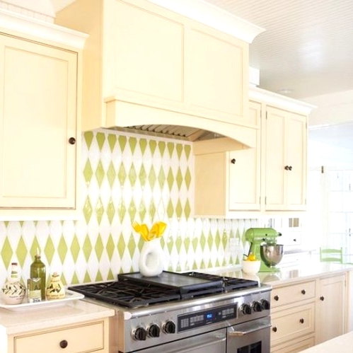 a vintage tan kitchen with a green and white geometric tile backsplash, with neutral countertops and green accessories to echo with the backsplash